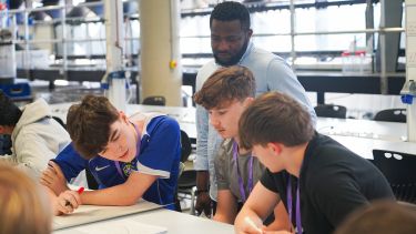 Three year 12 students working at a table as a an academic observes