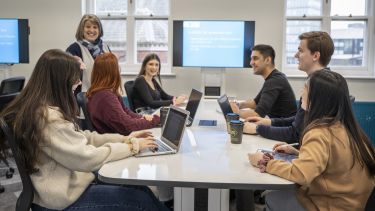 Photo of an academic teaching postgraduate students around a table 