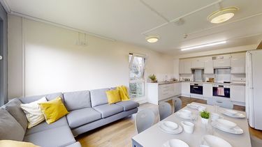 A large kitchen with a grey sofa and table with bowls and plates